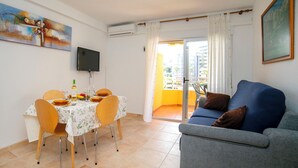 A living room with a dining table, chairs, a sofa, a TV, and a balcony with a view. - Voramar by Interhome (Calpe/Calp)