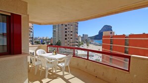 Ein Balkon mit Tisch und Stühlen, der Blick auf einen Strand und Gebäude freigibt.