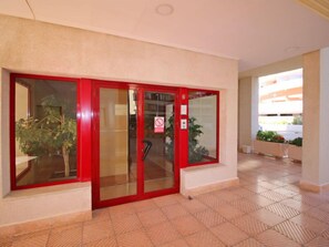 Entrada de hotel com porta vermelha, placa de proibido fumar e piso de azulejos.