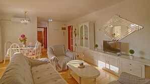 Ein Wohnzimmer mit einer Couch, Sesseln, einem Couchtisch, einem Fernseher und einer Vitrine.