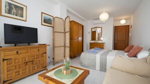 Une chambre d’hôtel de taille modeste, comprenant un lit, un canapé, une commode en bois, une télévision et un miroir.