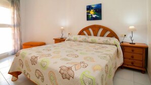 A bedroom with a bed, two bedside tables with lamps, a window with curtains, and a painting on the wall.