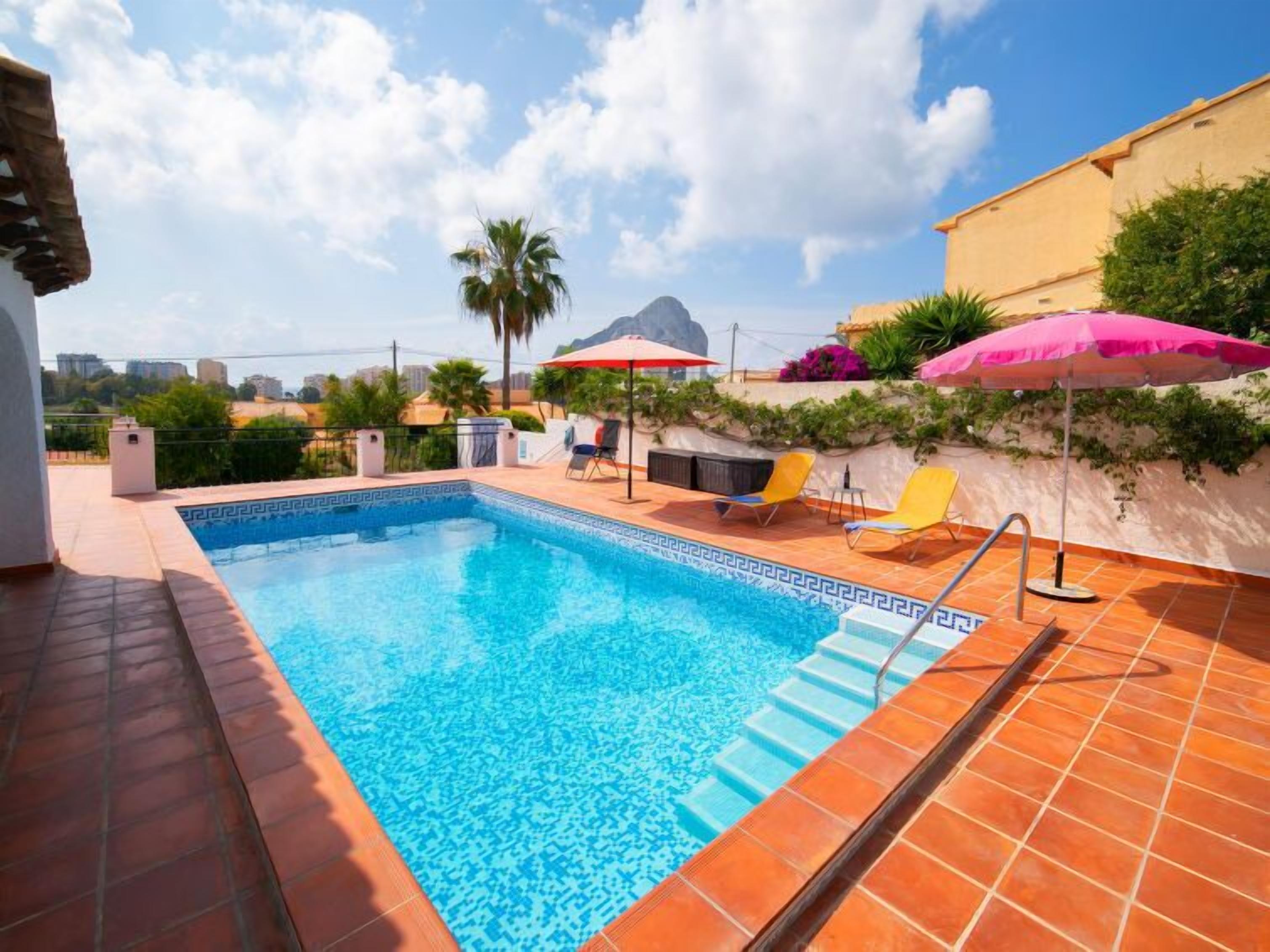 Ein Pool mit gefliesten Stufen, umgeben von einer Terrasse mit Liegestühlen und Sonnenschirmen.