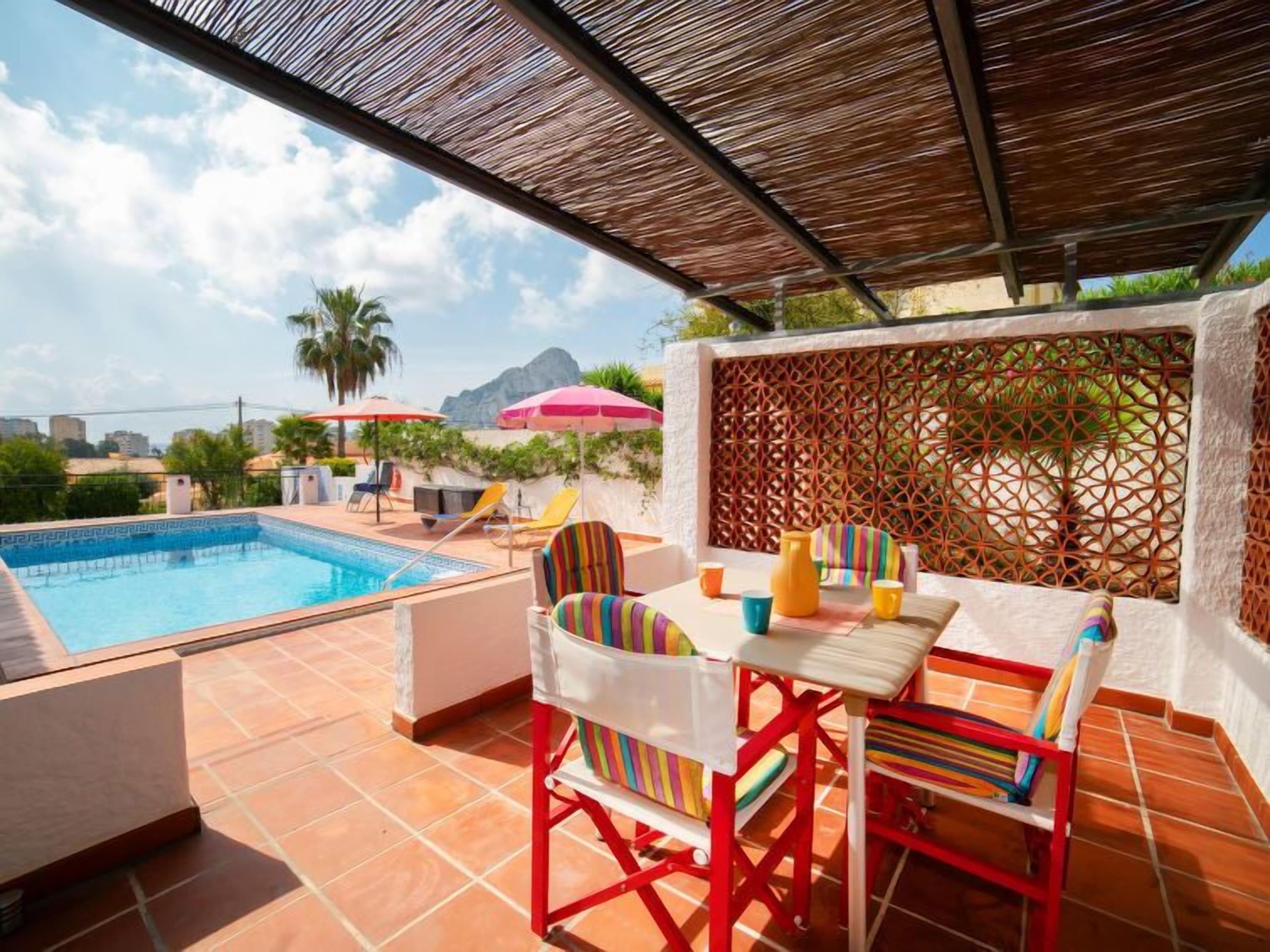 A poolside area with a tiled floor, a pool, and a table with chairs.