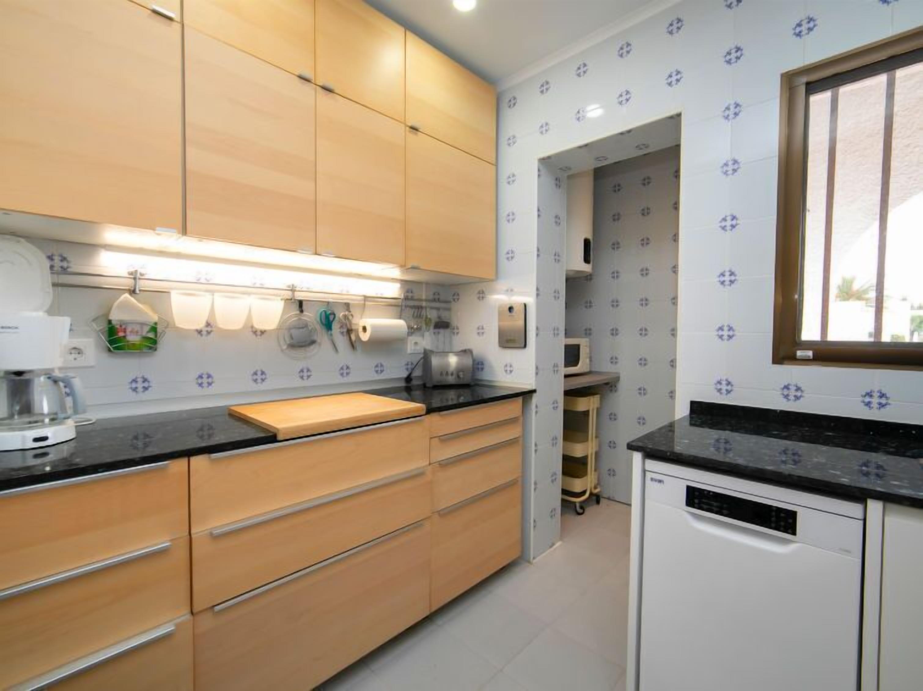 A modern kitchen with wooden cabinets, a black countertop, and a built-in dishwasher.