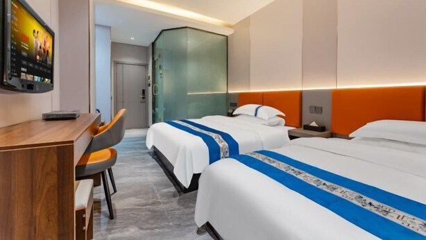 Quarto de hotel com duas camas, uma secretária e uma televisão.