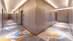Corredor moderno de hotel com carpete estampado, iluminação embutida e design simétrico.