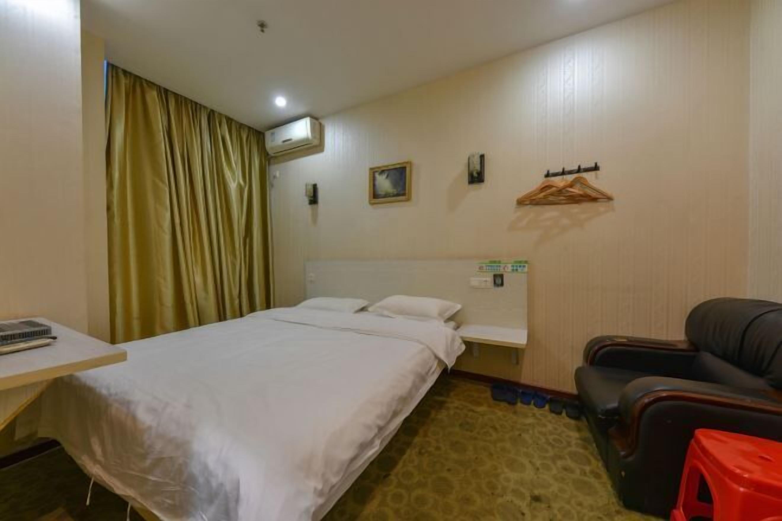 A hotel room with a bed, a desk with a chair, a massage chair, and a coat rack with hangers.