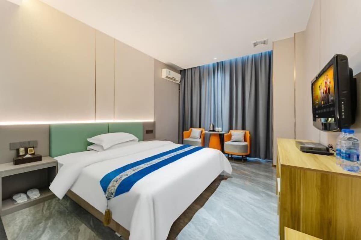A hotel room with a bed, a desk with a television, a chair, and a window with curtains.