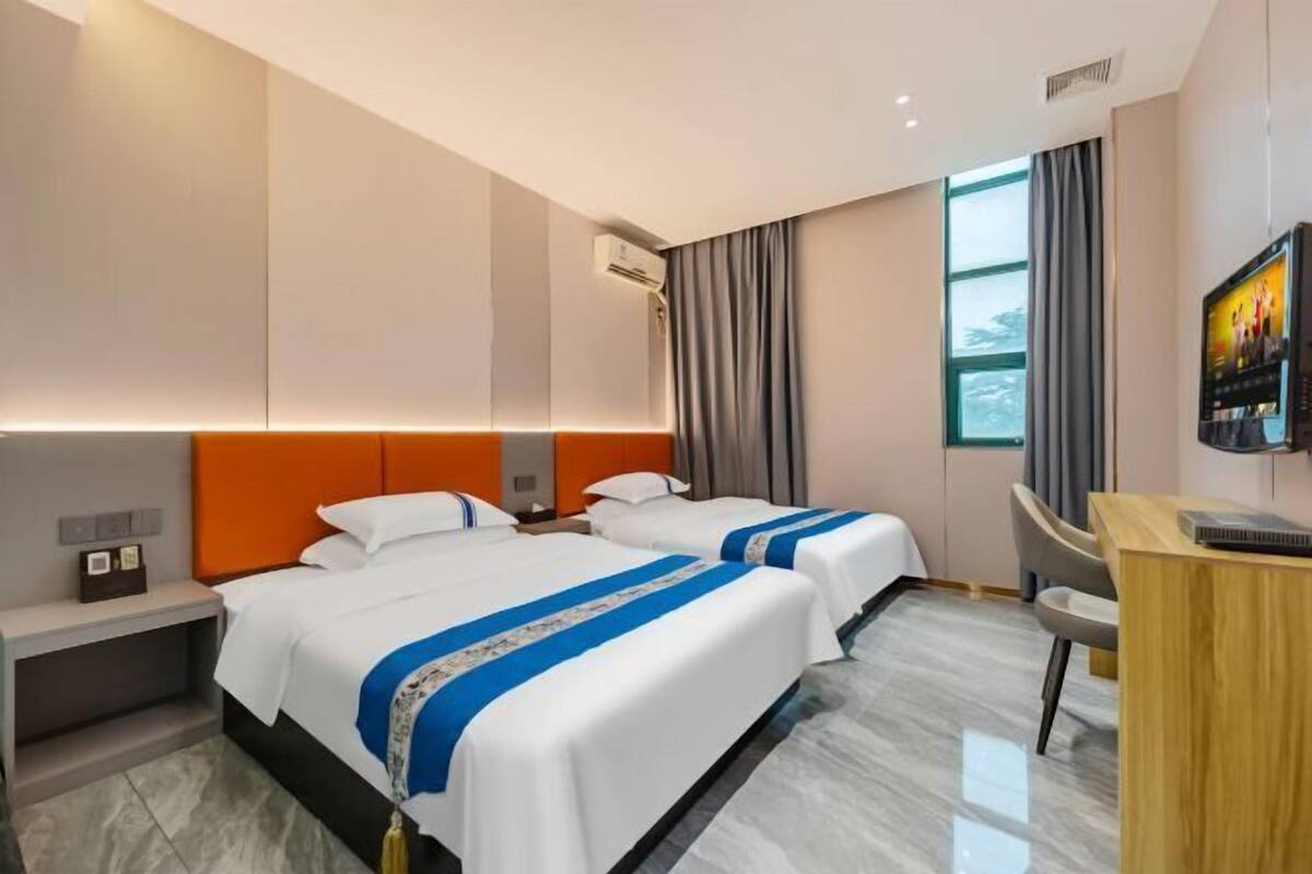 Une chambre d’hôtel avec deux lits, un bureau, une télévision et une fenêtre avec des rideaux.