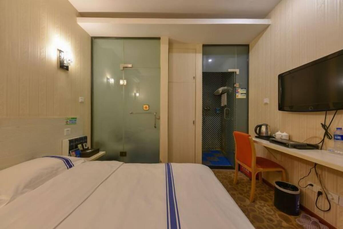 Une chambre d’hôtel avec deux lits, un bureau avec une télévision, un espace douche et une petite poubelle.