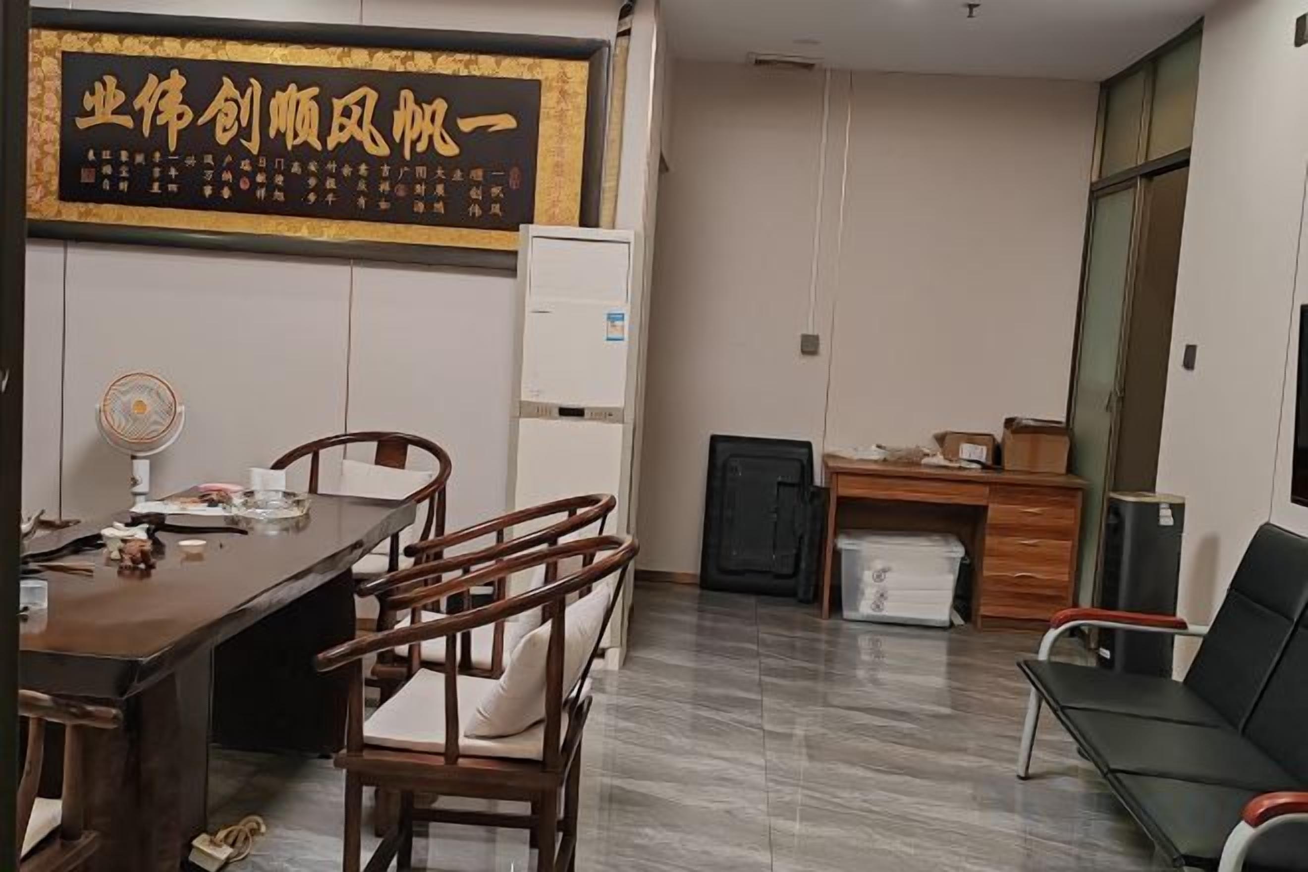 Sala de conferências com mesa de madeira, cadeiras, quadro branco e um frigorífico pequeno.