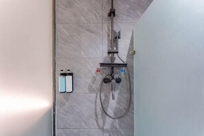 Eine Dusche mit Duschbrause, Wandarmatur sowie zwei Flaschen Shampoo und Conditioner.
