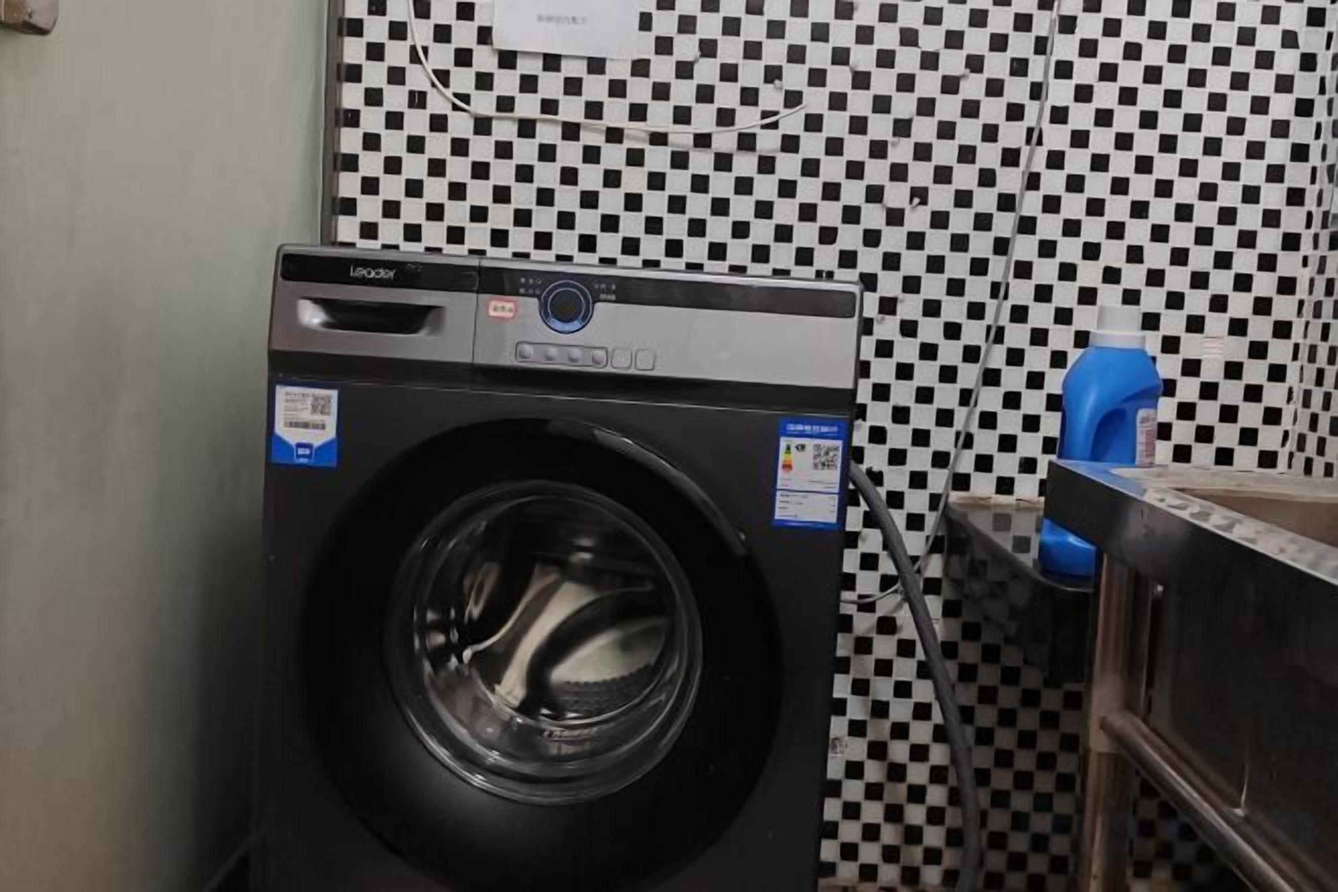 A front-loading washing machine in a laundry room with a checkered wall pattern.