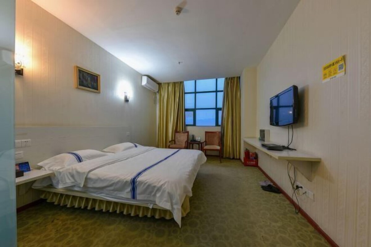 Ein Hotelzimmer mit zwei Betten, einem Schreibtisch mit Computer, einem Fernseher und einem Fenster mit Vorhängen.