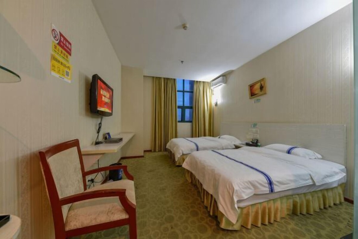 Ein Hotelzimmer mit zwei Betten, einem Schreibtisch, einem Sessel, einem Fernseher und einem Fenster mit Vorhängen.