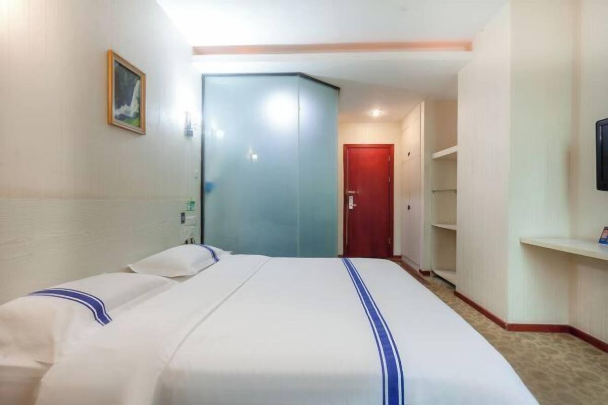Une chambre d’hôtel avec un lit, une porte, un téléviseur fixé au mur et un tableau.