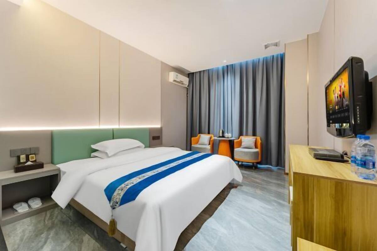 Une chambre d’hôtel avec un lit, un bureau, une télévision et une fenêtre avec des rideaux.