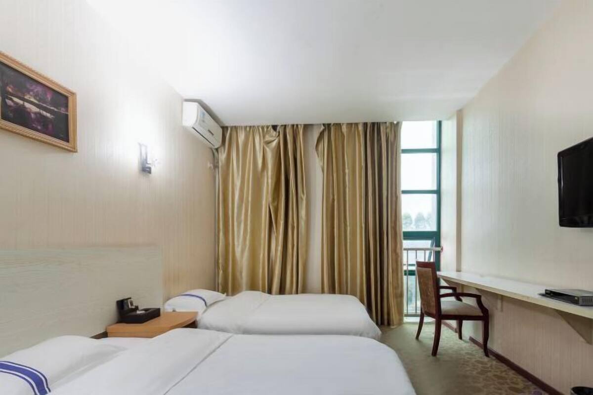 Une chambre d’hôtel avec deux lits, un bureau, une chaise, une télévision et une fenêtre avec des rideaux.