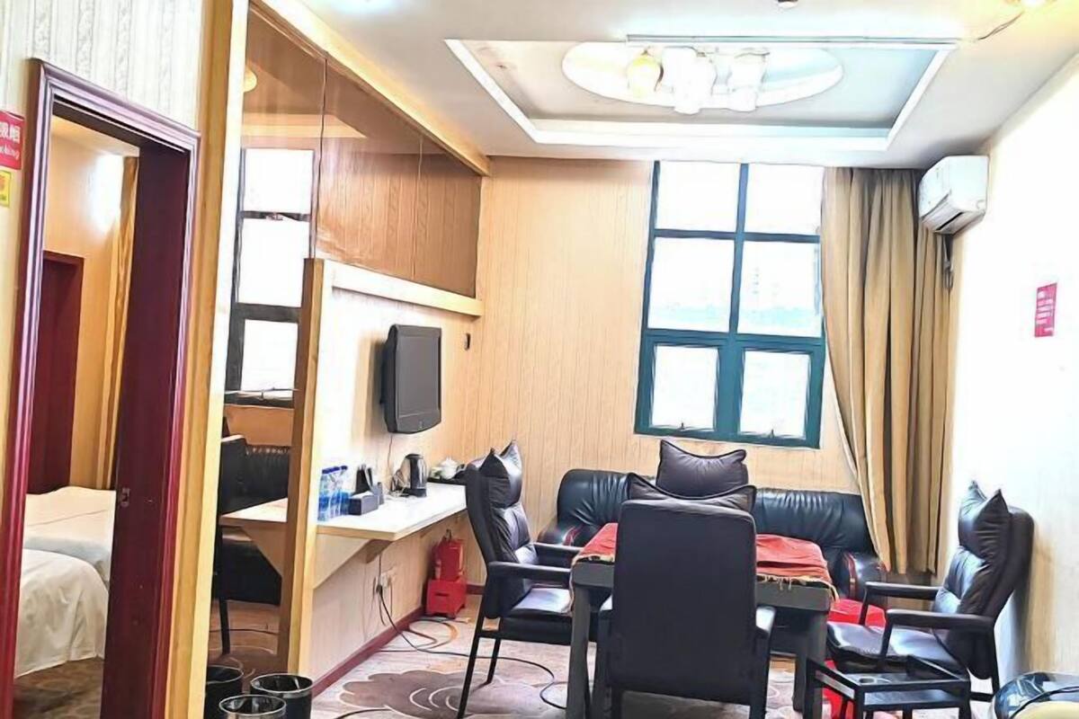 Une chambre d’hôtel de taille réduite comprenant un lit, un bureau avec une chaise, un canapé avec des coussins, une télévision et une fenêtre avec des rideaux.