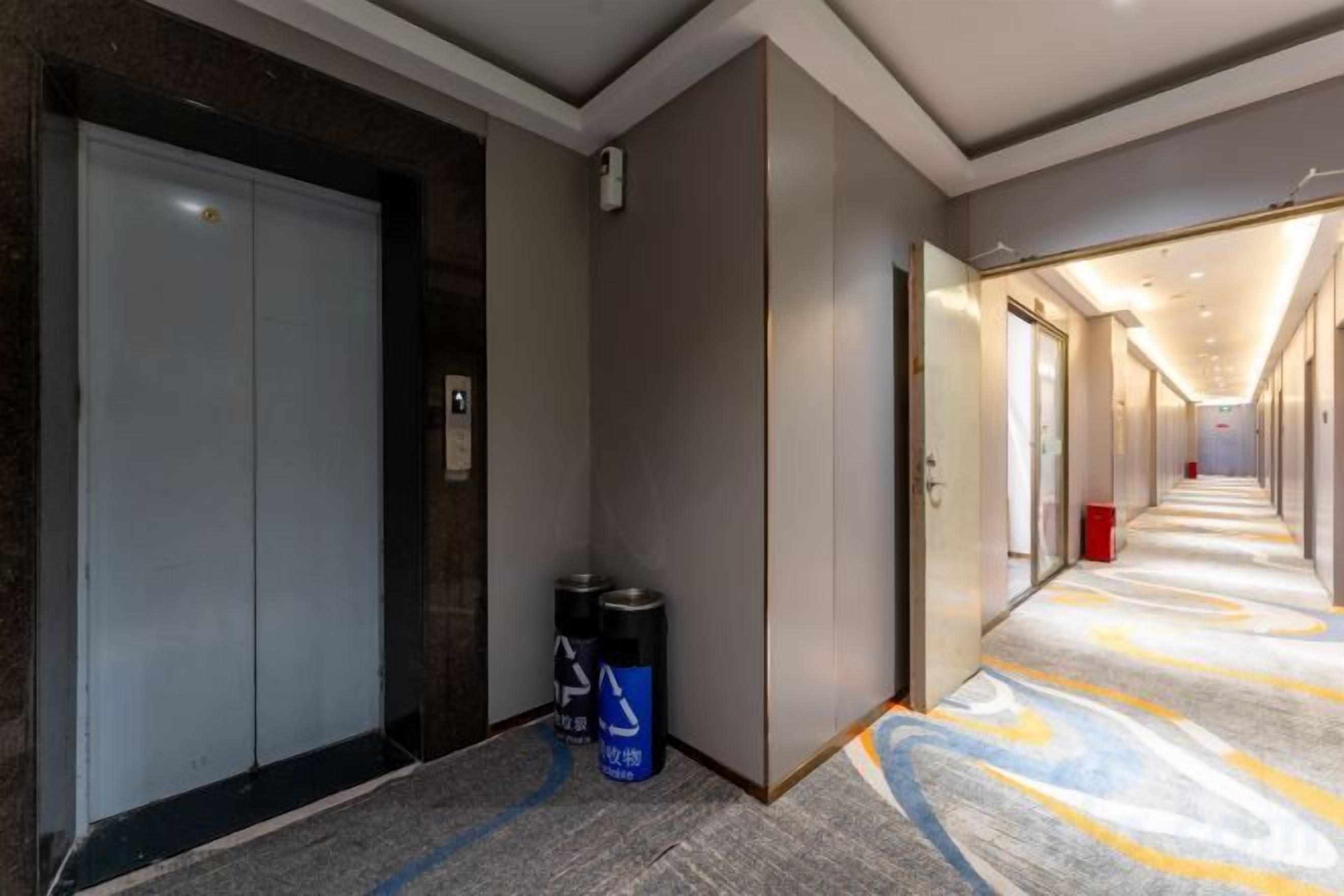 Corredor de hotel com piso de carpete, elevador fechado e lixeira.