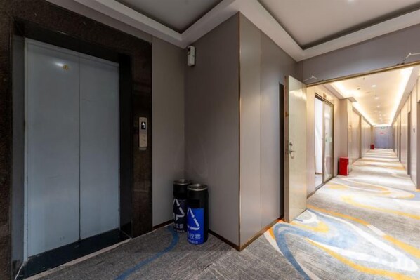 A hotel corridor with a carpeted floor, a closed elevator, and a trash bin.