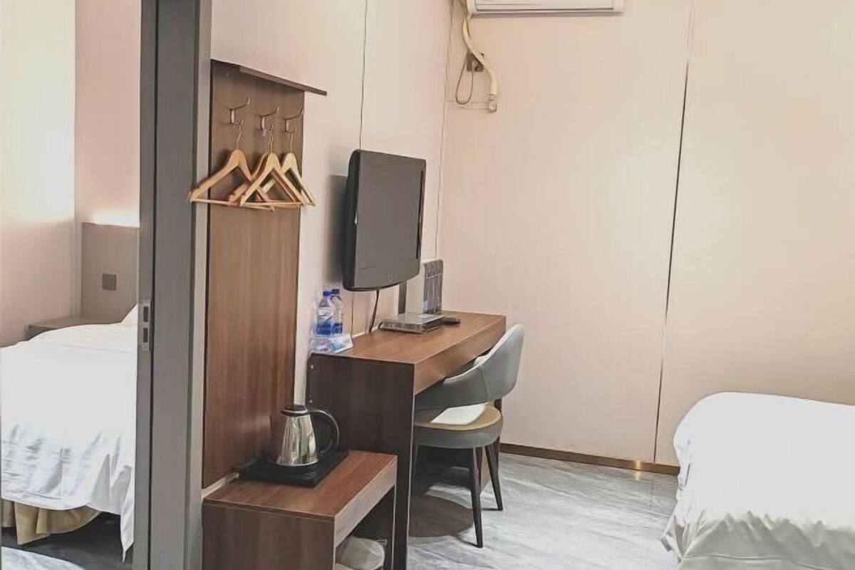 Une chambre d’hôtel avec deux lits, une armoire en bois, un bureau avec une chaise, une télévision et une bouilloire.