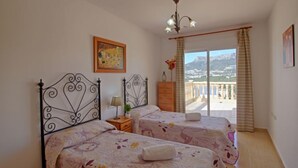 Ein Schlafzimmer mit zwei Betten, einer Chandelieber, einem Gemälde und einem Balkon mit Bergblick.