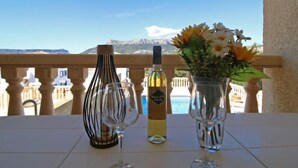 Ein Tisch mit einer Weinflasche, zwei Weingläsern und einem Blumenstrauß auf einem Balkon mit Blick auf eine schöne Landschaft.