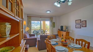 Ein Essbereich mit einem Holztisch, gedeckt für vier Personen, einer Couch und einem Balkon mit Blick.