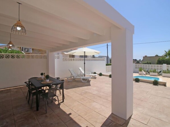 An outdoor patio with a dining table and chairs, a pool, and lounge chairs.