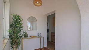 En gang med en potteplante, et konsolbord med et spejl og en dekorativ loftlampe.