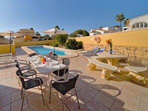 A poolside area with a table set for dining, lounge chairs, and a stone fountain. - Villa Acuario by Interhome (Calpe/Calp)