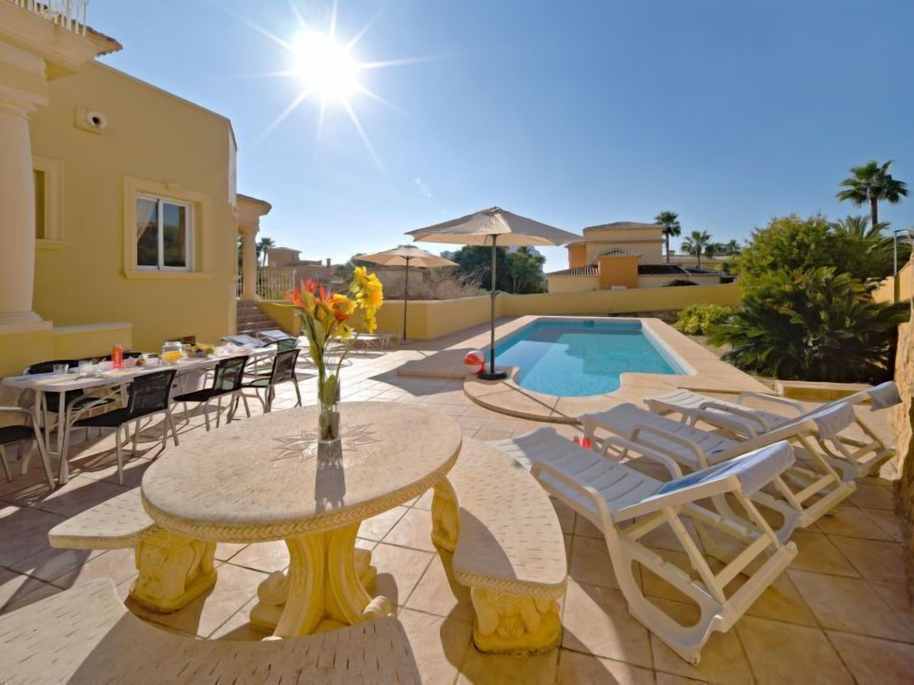 Un espace aménagé au bord de la piscine, avec une table ronde, des chaises longues et un parasol.