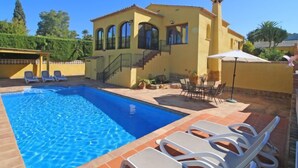 A yellow villa with a swimming pool, outdoor seating, and a staircase leading to the upper floor.