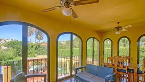 A bright room with large windows, a ceiling fan, and a dining area with wooden furniture.