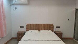 A bedroom with a wooden headboard, a bed with white bedding, two bedside tables, and an air conditioning unit on the wall. - Shengsi Haiwang Mingzhu Homestay (Shengsi)
