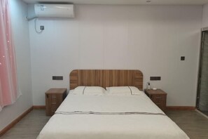 A bedroom with a wooden headboard, a bed with white bedding, two bedside tables, and an air conditioning unit on the wall.