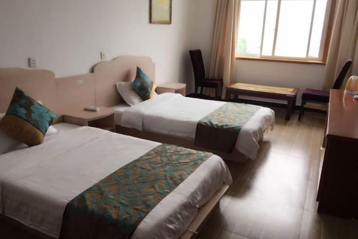 Quarto de hotel com duas camas, uma escrivaninha e uma cadeira.