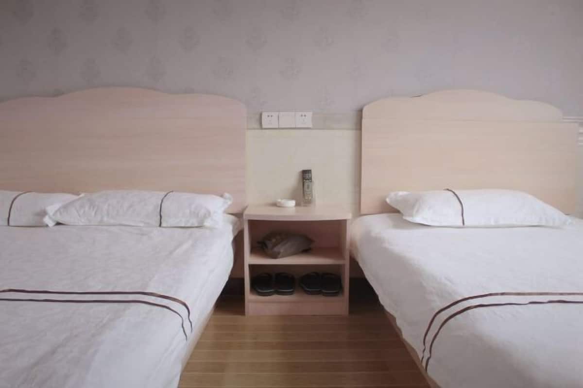 Quarto de hotel com duas camas de solteiro, uma mesa de cabeceira com abajur e um sapateiro.