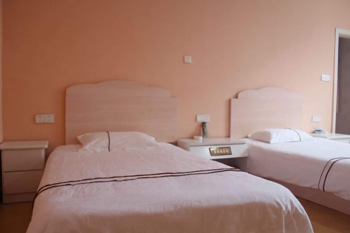 Quarto de hotel com duas camas, mesa de cabeceira, luminária e relógio na parede.
