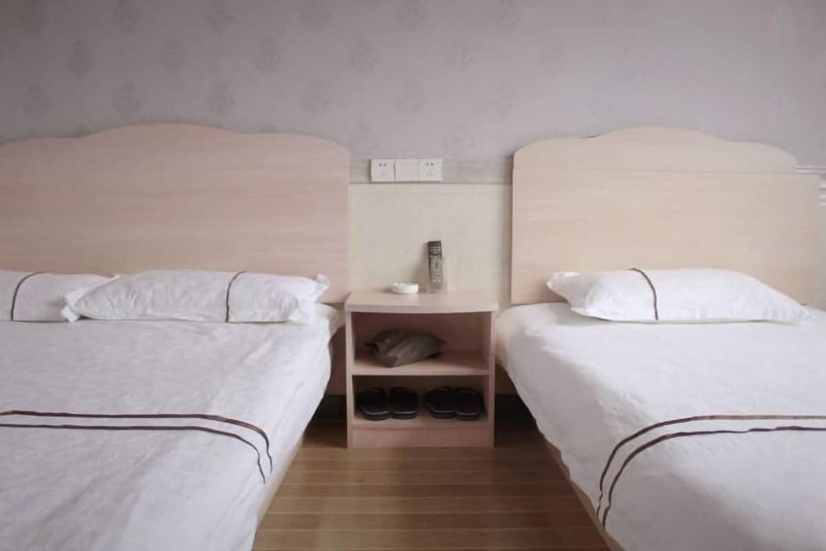 Quarto de hotel com duas camas de solteiro, uma mesa de cabeceira com abajur e um sapateiro.