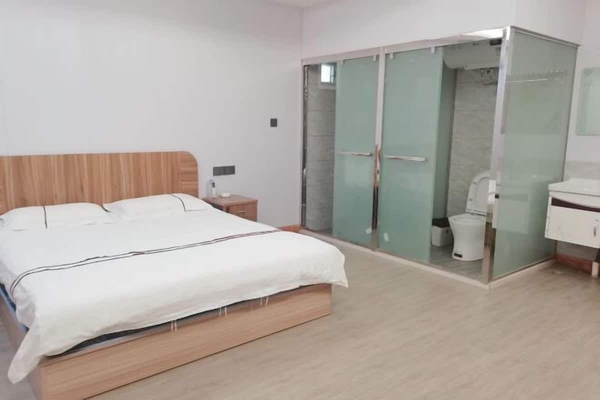 Quarto com cama, mesa de cabeceira e área de chuveiro com paredes de vidro.