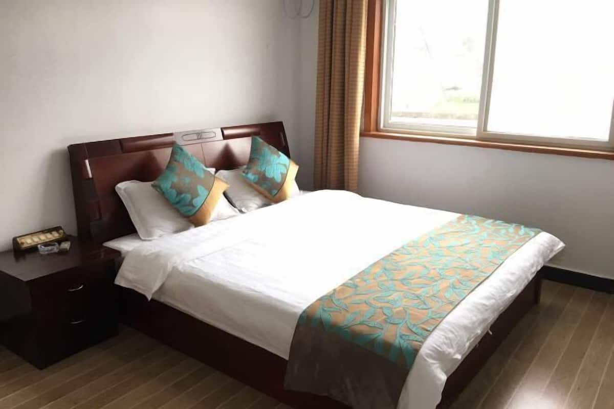 Uma cama bem arrumada com colcha estampada, cabeceira de madeira e mesa de cabeceira com abajur e relógio.