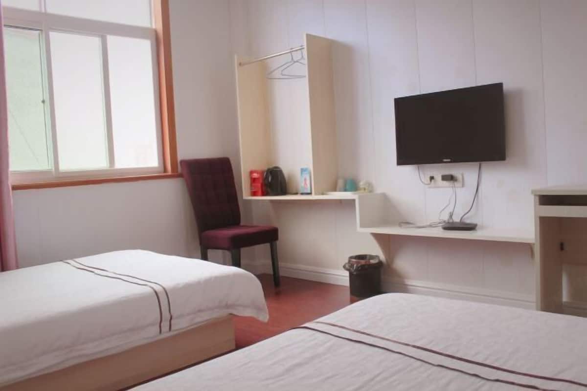 Quarto de hotel com duas camas, televisão, escrivaninha, cadeira e guarda-roupa.