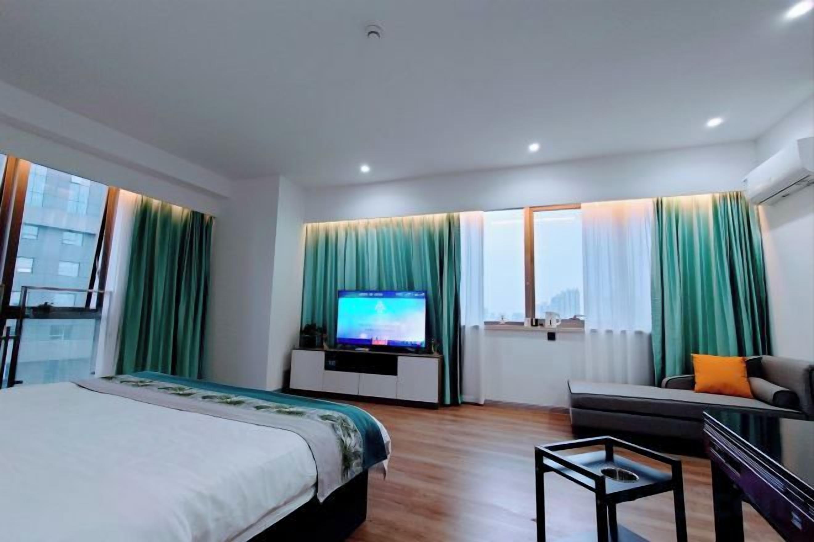 A hotel room with a bed, a TV, a sofa, and a window with curtains.