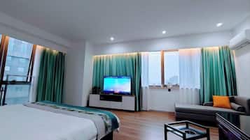 A hotel room with a bed, a TV, a sofa, and a window with curtains.