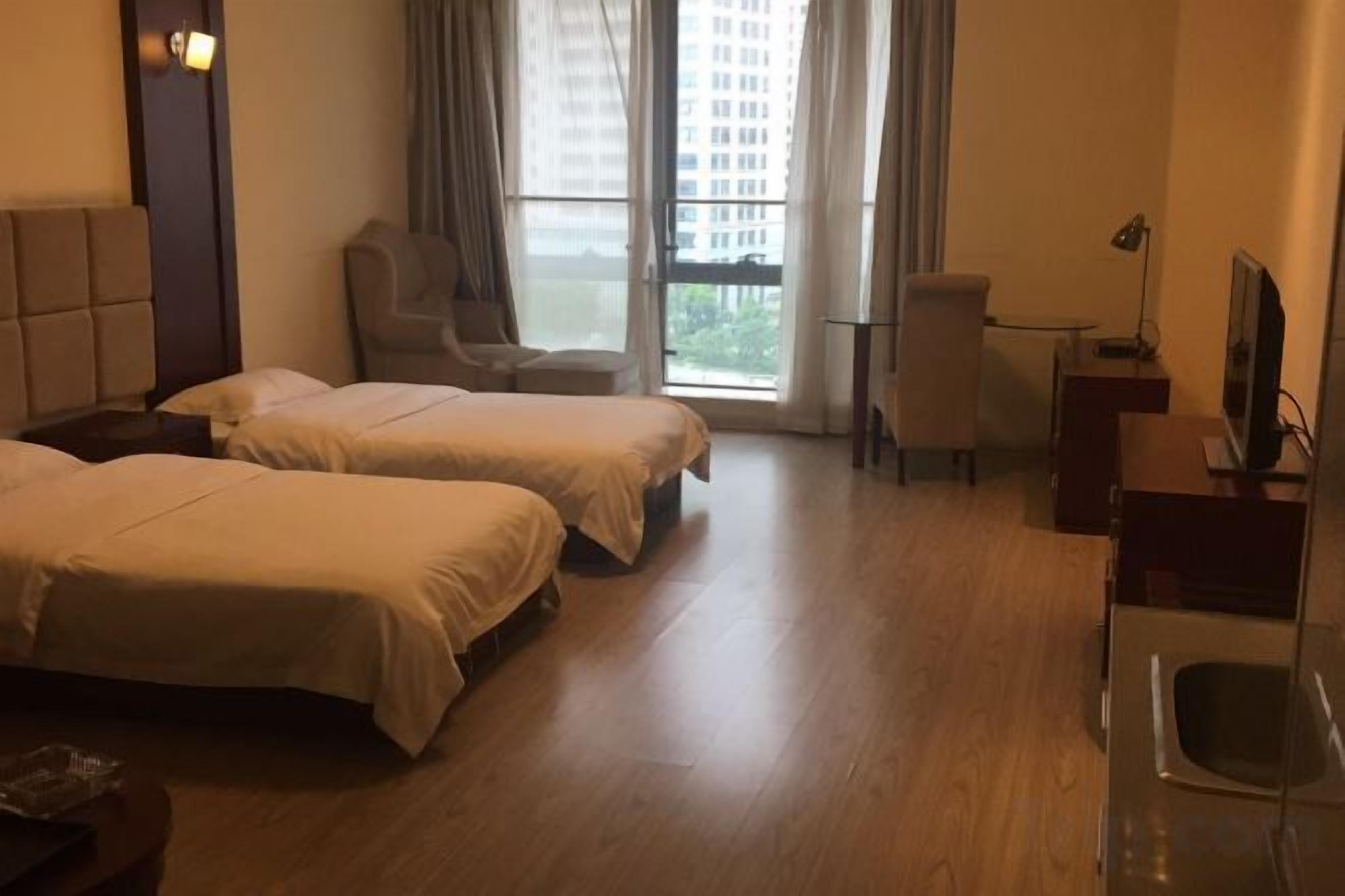 A hotel room with two beds, a desk, a chair, a television, and a window with curtains.