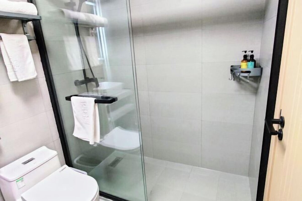 Une cabine de douche fermée par des parois en verre, avec des toilettes blanches et un porte-serviettes.