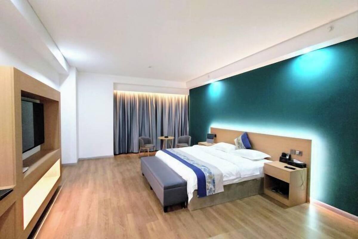 Une chambre d’hôtel moderne équipée d’un lit, d’une table de chevet, d’une télévision et d’un coin salon avec des fauteuils.